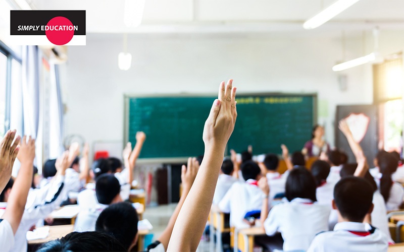 Students raising their hands in a classroom, actively engaging in a lesson.
