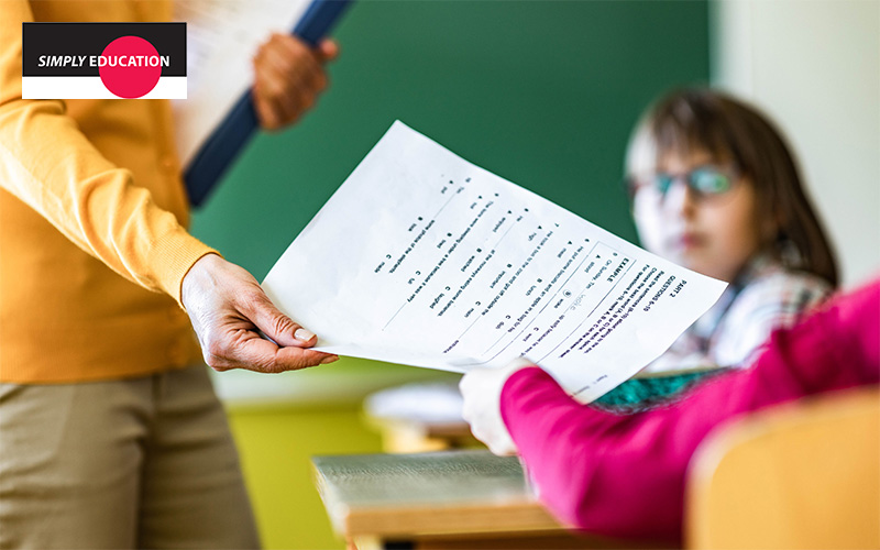 A teacher handing a test paper to a student in a classroom.