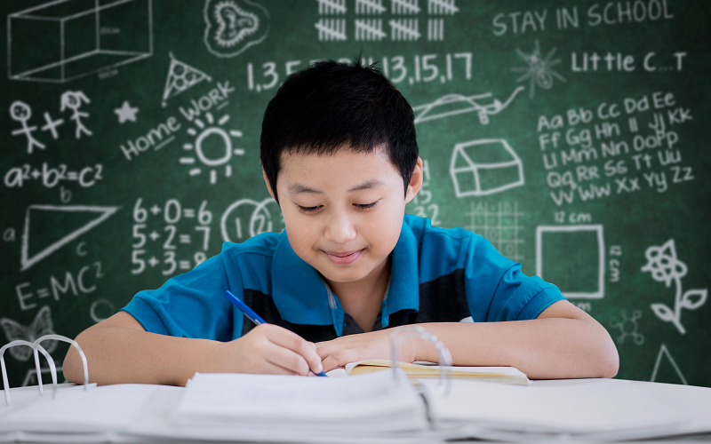 Primary student practicing math problem solving in front of chalkboard.