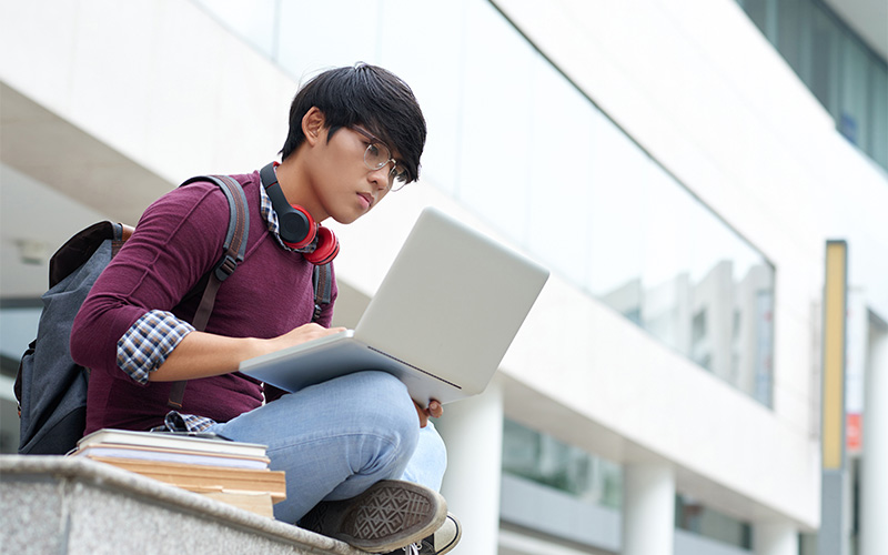 A student using a laptop to research and expand their vocabulary beyond standard model essay templates.
